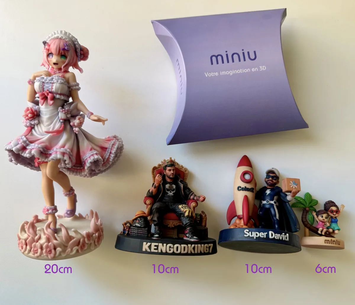 Photo d'atelier de quatre vraies figurines Miniu imprimées en 3D, de 20 cm, 10 cm et 6 cm, posées à côté d'une boîte Miniu pour l'échelle