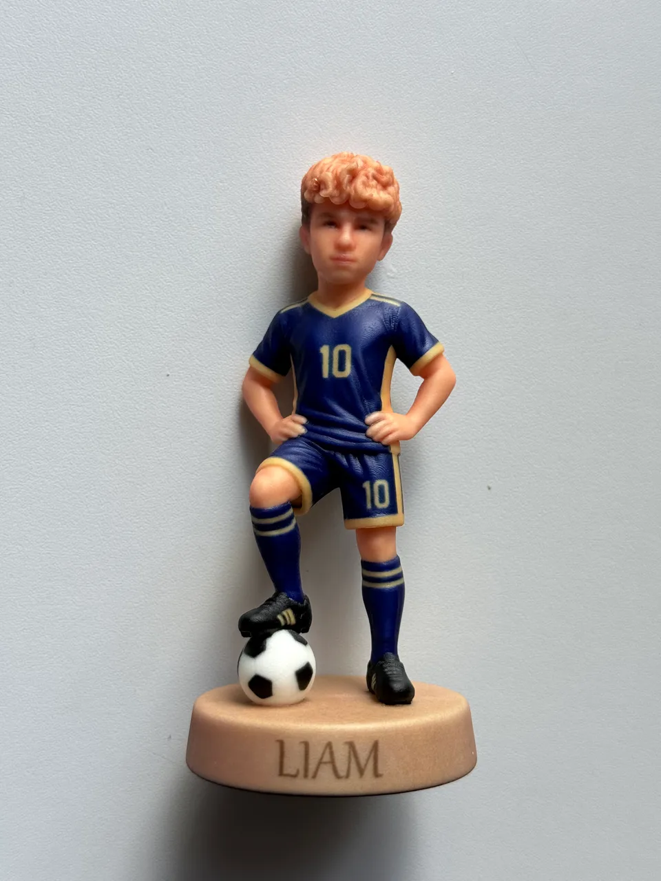 Figurine imprimée de 10 cm d'un jeune footballeur roux en maillot bleu et or numéro 10, pied sur le ballon